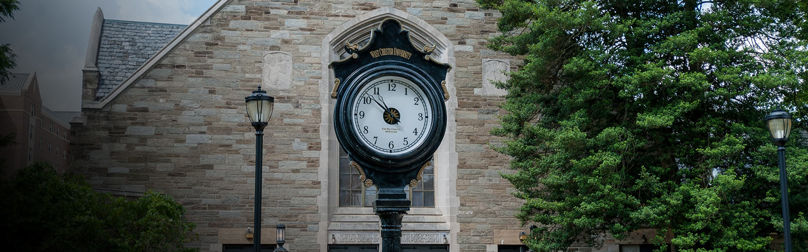 Black West Chester University clock in front of an old brick building