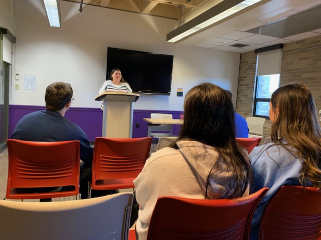 3 students looking at woman standing at podium